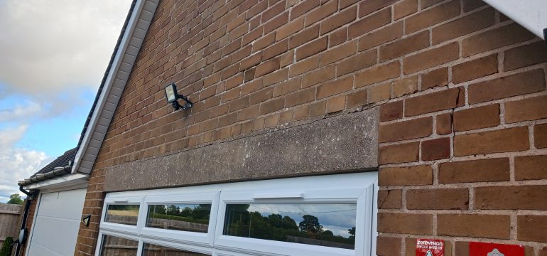 A brick wall of a house with a white garage door, an outdoor security light, and a cloudy sky in the background.