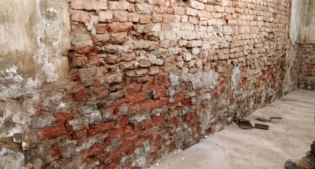 Stripped solid brick wall showing moisture saturation and salt deposits undergoing a natural drying process.